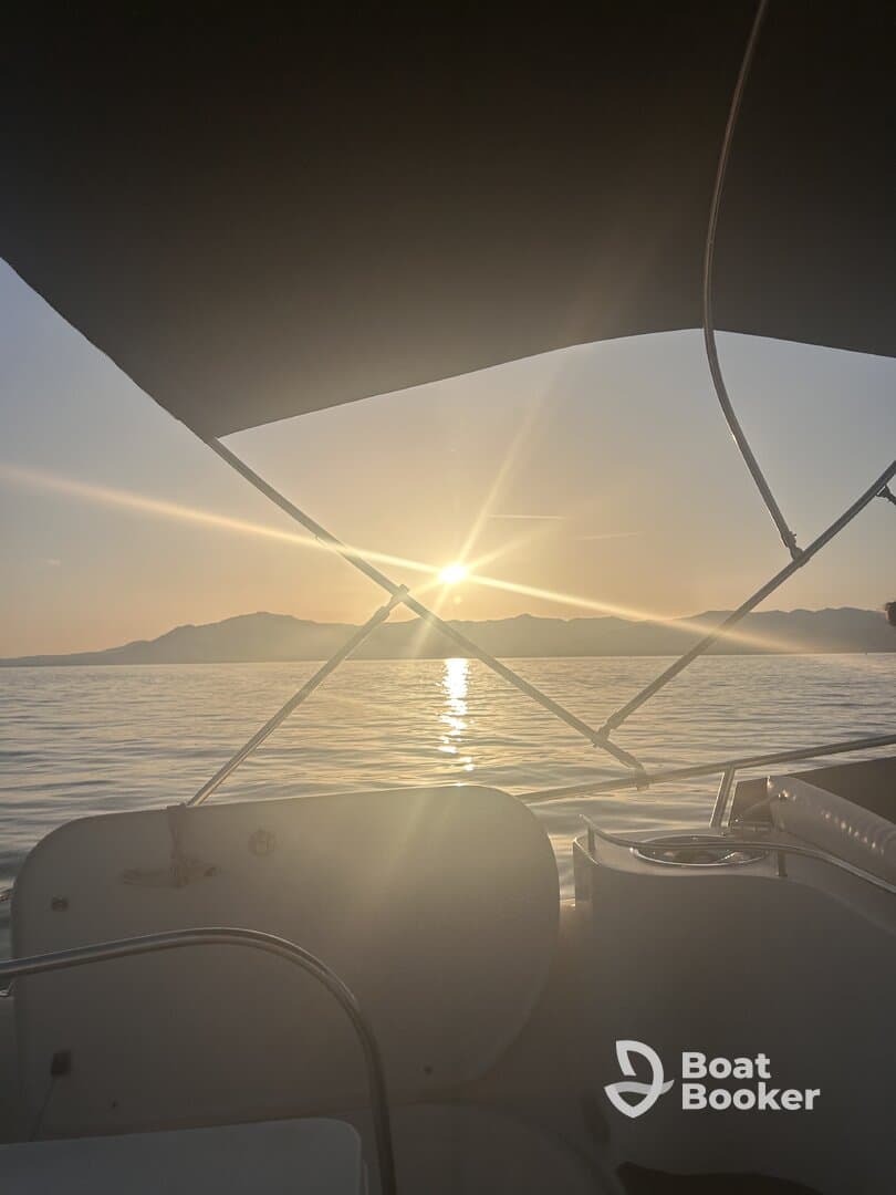 A serene sunset view from the deck of a boat, showcasing the tranquil waters and distant mountains — perfect for evening cruises.