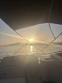 A serene sunset view from the deck of a boat, showcasing the tranquil waters and distant mountains — perfect for evening cruises.