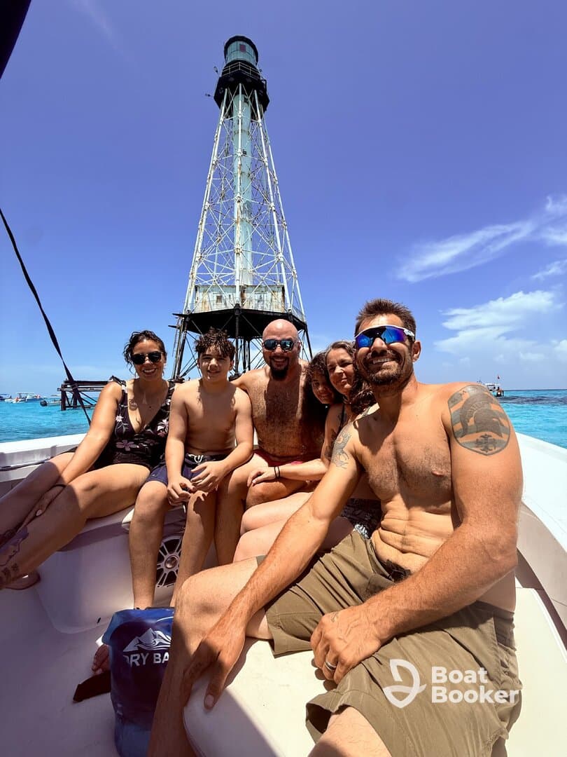 A joyful group poses for a selfie on a boat near a lighthouse, capturing a memorable moment during their aquatic adventure.