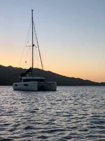 A serene view of a catamaran anchored at sunset, surrounded by tranquil waters and mountains, perfect for a peaceful evening on the water.