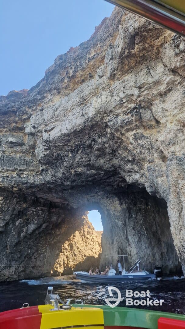 A scenic view of a boat navigating through a natural rock arch, showcasing the stunning coastline and adventure on the water.