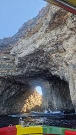 A scenic view of a boat navigating through a natural rock arch, showcasing the stunning coastline and adventure on the water.