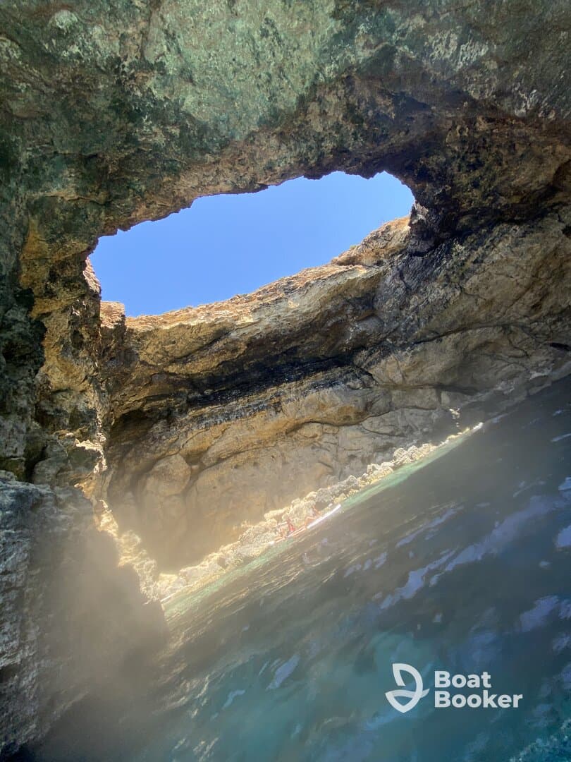 A stunning view from inside a cave, showcasing the natural rock formations and a glimpse of kayakers enjoying the serene waters — a perfect spot for adventure seekers.