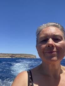 A woman enjoys a sunny day on the water, capturing the beautiful scenery behind her while on a boat trip — a perfect moment for adventure seekers.