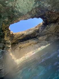 A stunning view from inside a cave, showcasing the natural rock formations and a glimpse of kayakers enjoying the serene waters — a perfect spot for adventure seekers.
