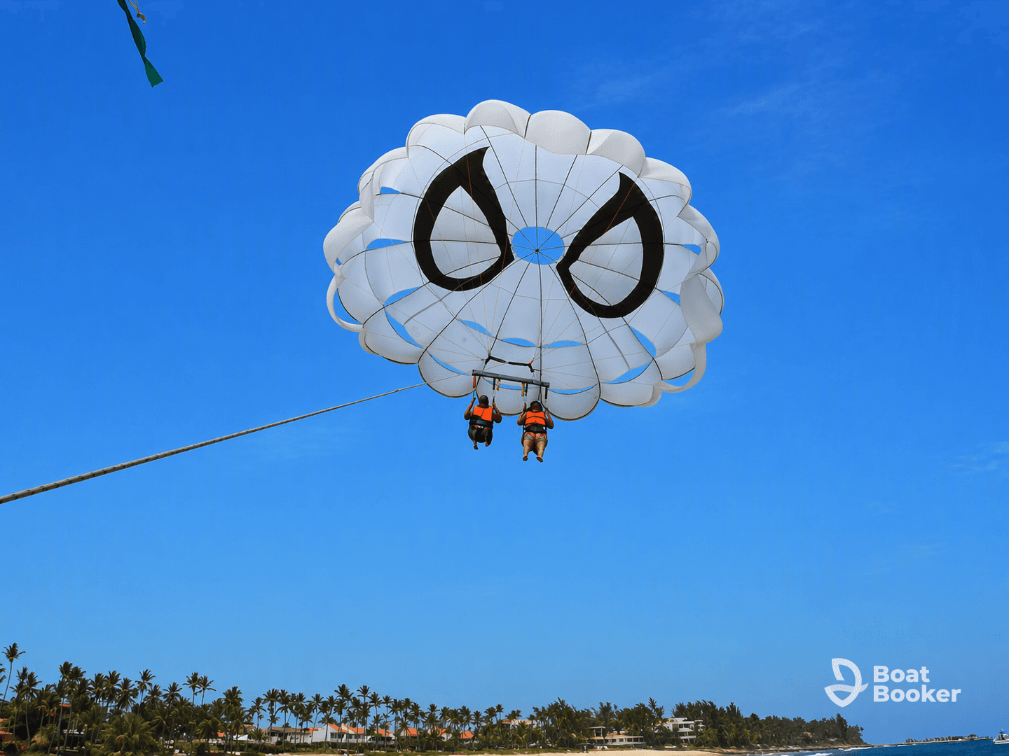 Two adventurers enjoy an exhilarating parasailing experience over the ocean, offering stunning views of the coastline and beach below.