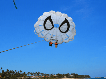 Two adventurers enjoy an exhilarating parasailing experience over the ocean, offering stunning views of the coastline and beach below.