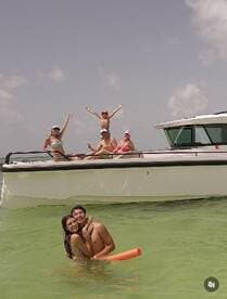 A joyful group enjoys a fun day on the water, celebrating with swimming and laughter around a pontoon boat — perfect for family outings and summer adventures.