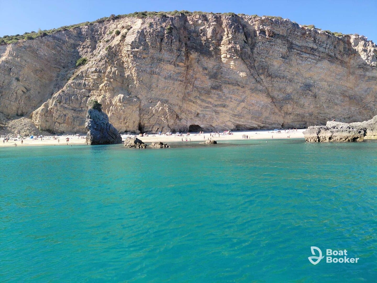 A stunning view of a beach with people enjoying the sun and swimming, framed by dramatic cliffs and clear turquoise waters — an ideal destination for relaxation and adventure.