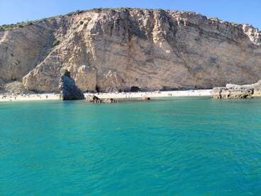 A stunning view of a beach with people enjoying the sun and swimming, framed by dramatic cliffs and clear turquoise waters — an ideal destination for relaxation and adventure.