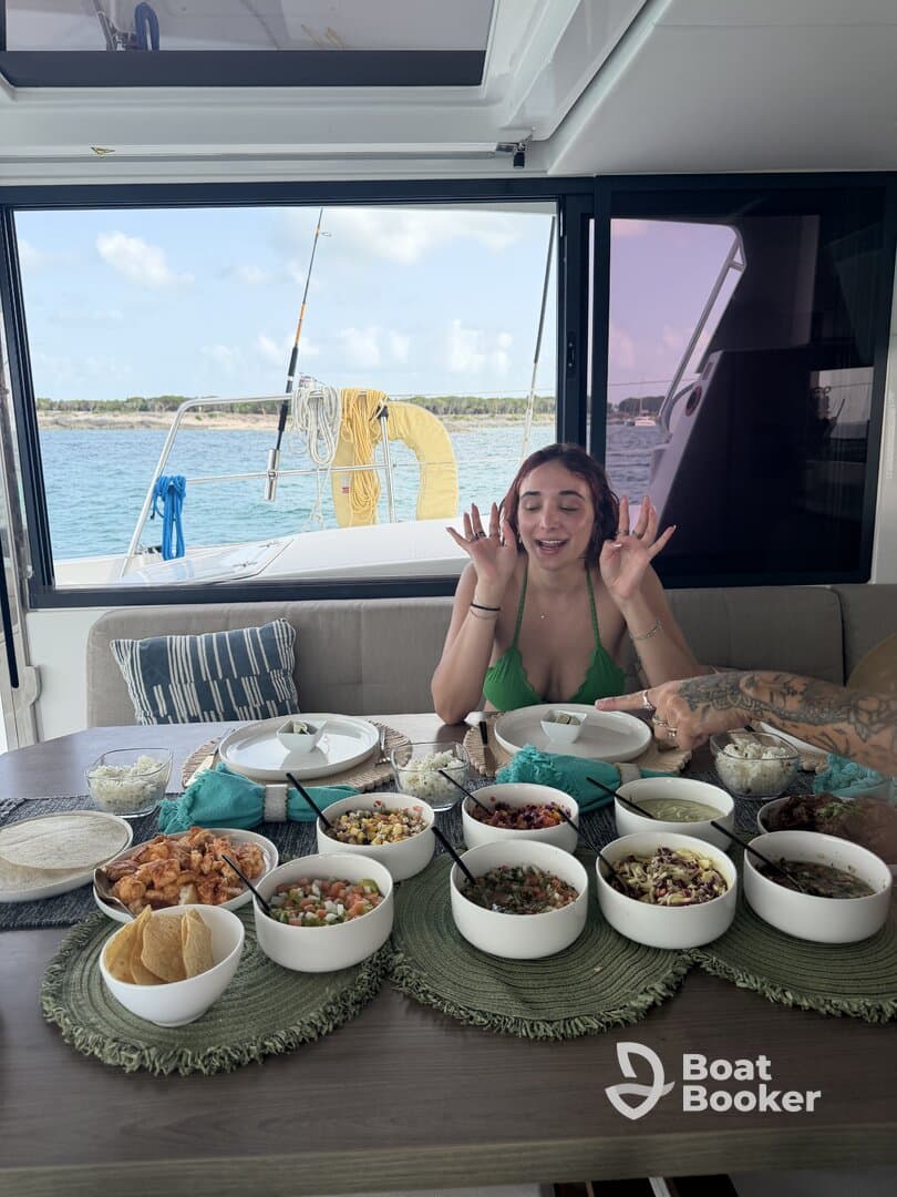 A vibrant spread of delicious food is laid out on a dining table aboard a boat, with a guest excitedly enjoying the meal — perfect for onboard catering experiences.