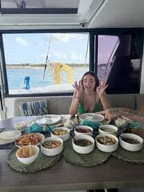 A vibrant spread of delicious food is laid out on a dining table aboard a boat, with a guest excitedly enjoying the meal — perfect for onboard catering experiences.