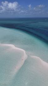 A stunning aerial view of a sandbar with people walking along the shoreline, surrounded by crystal-clear turquoise waters — a perfect tropical getaway.