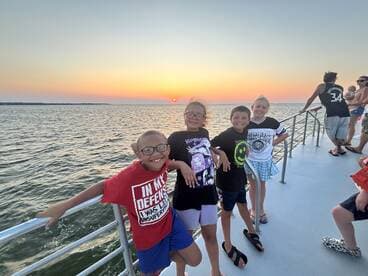 A joyful group of children poses for a photo on a boat during a stunning sunset, capturing the essence of fun and adventure on the water.