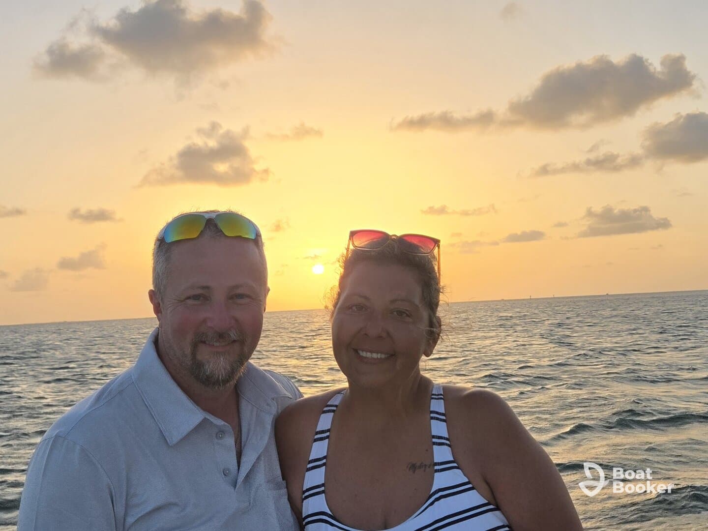 A couple smiles together against a stunning sunset backdrop on the water, capturing a perfect moment of romance and celebration.