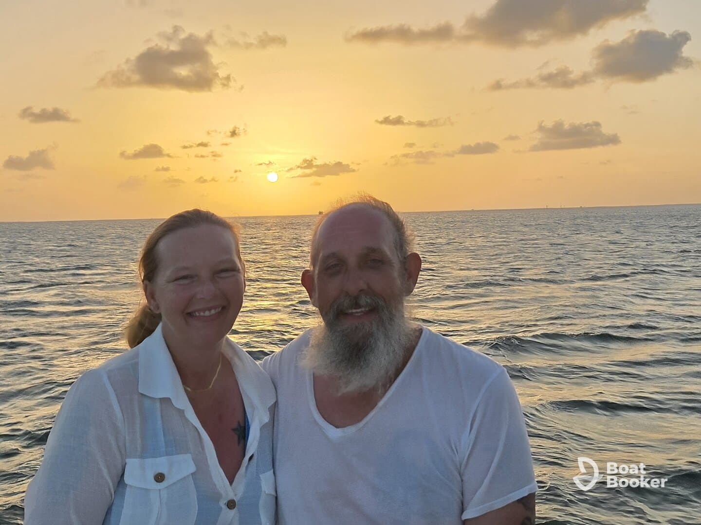 A couple smiles together against a stunning sunset backdrop, capturing a romantic moment on the water — perfect for anniversary celebrations or sunset cruises.