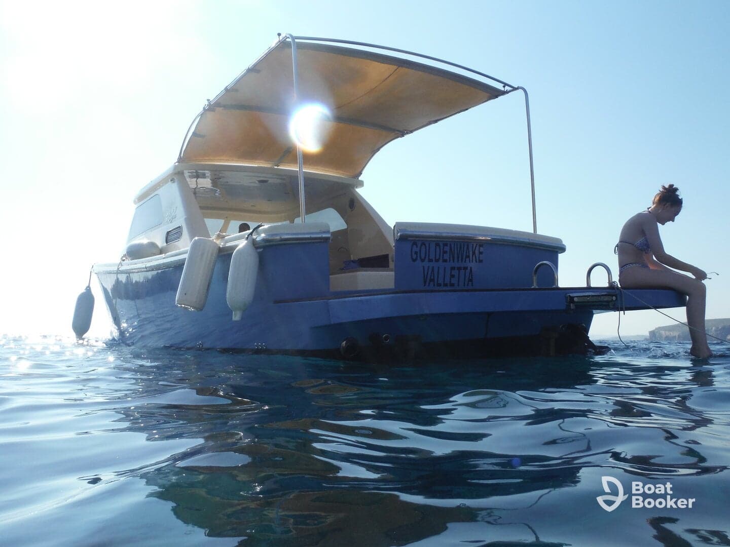 A girl relaxes on the edge of a boat named 'Goldenwake Valletta,' enjoying the serene waters — a perfect moment for summer adventures.
