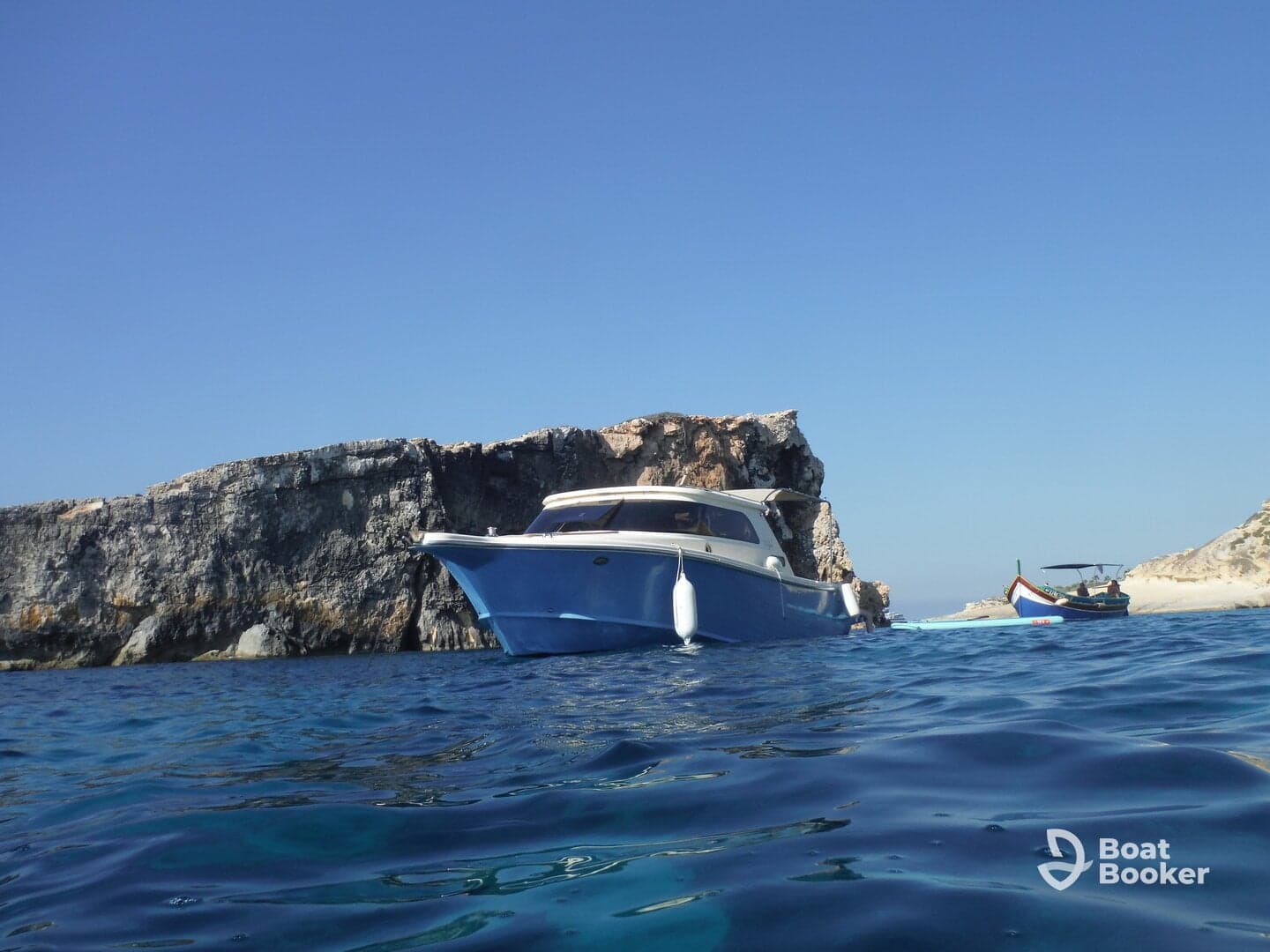 A beautiful blue boat is anchored near a rocky coastline, showcasing the serene waters and clear skies — perfect for a day of exploration.