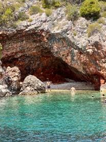 A group enjoys a refreshing swim in crystal-clear waters near a stunning rocky cave, perfect for adventure seekers and beach lovers.