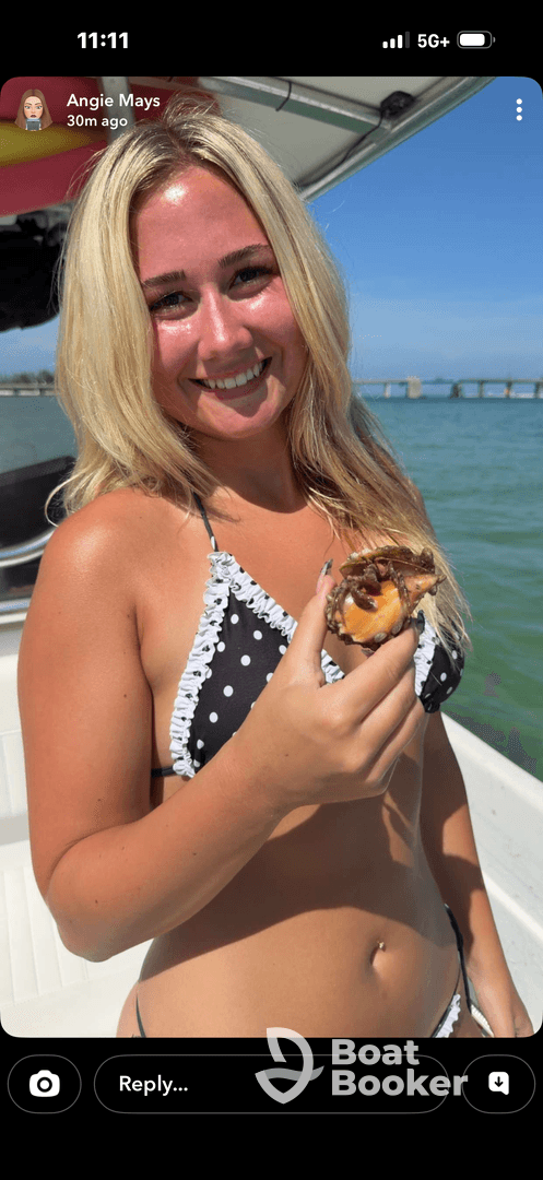 A young woman enjoys a freshly shucked oyster while smiling on a boat under the sun — a perfect moment for seafood lovers on a sunny day out on the water.