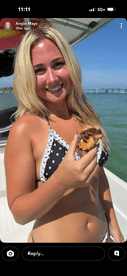 A young woman enjoys a freshly shucked oyster while smiling on a boat under the sun — a perfect moment for seafood lovers on a sunny day out on the water.
