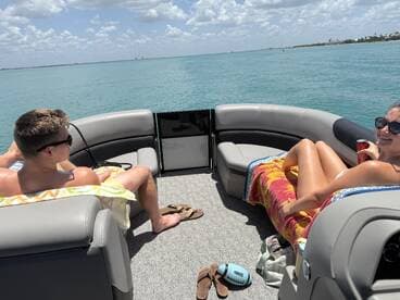 A couple enjoys a relaxing day on a pontoon boat, sipping drinks and soaking up the sun on the water — perfect for a summer getaway.