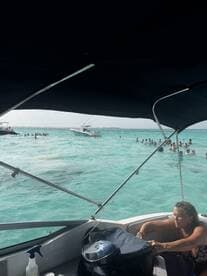 A lively scene captures guests enjoying the turquoise waters, with a woman relaxing on the boat while others swim nearby — a perfect day for water activities.