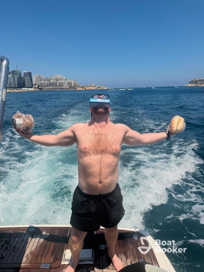 A man joyfully celebrates on a boat, holding bread and wearing snorkeling gear, capturing the essence of fun and adventure on the water.
