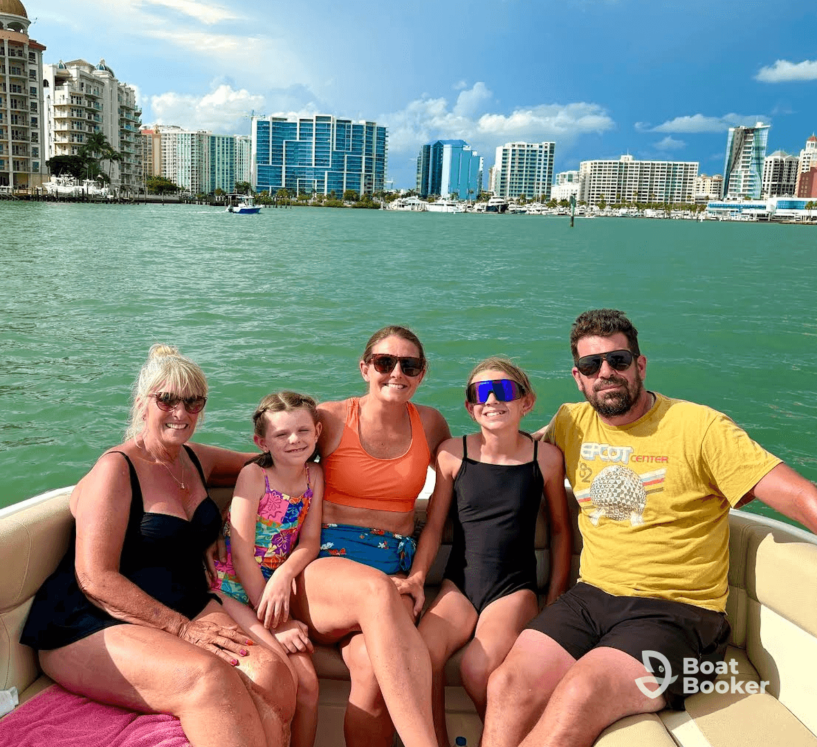 A joyful family enjoys a sunny day on the boat, capturing fun moments together against a vibrant city backdrop — perfect for family outings on the water.