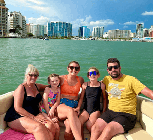 A joyful family enjoys a sunny day on the boat, capturing fun moments together against a vibrant city backdrop — perfect for family outings on the water.