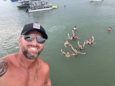 A lively group enjoys a fun day swimming in the water, with boats anchored nearby — perfect for summer parties and water adventures.