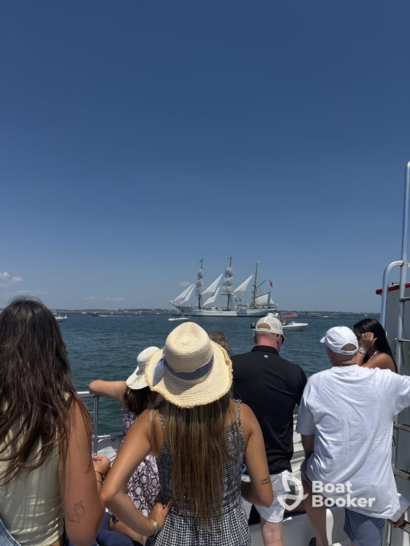 A group of guests enjoys a scenic view of a majestic sailing ship while aboard their own vessel, capturing the essence of a perfect day on the water.