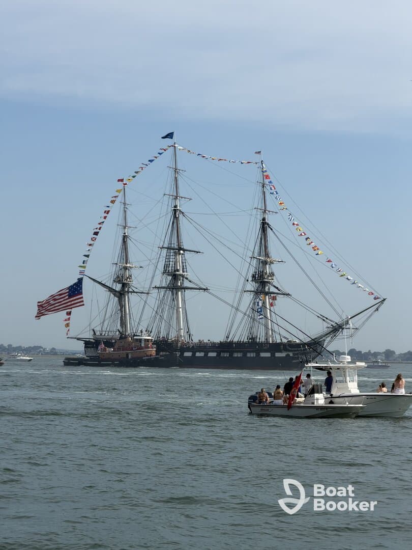A historic sailing ship adorned with flags navigates the waters, with a group of people enjoying the view from a nearby boat — a perfect scene of maritime celebration.