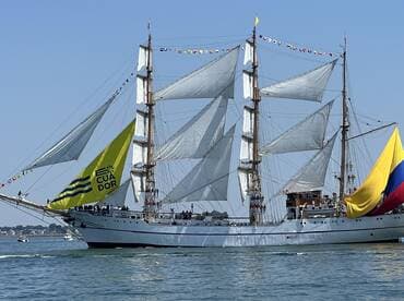 A majestic sailing ship adorned with vibrant flags and the Ecuadorian banner, gracefully navigating the waters — a stunning display of maritime tradition.