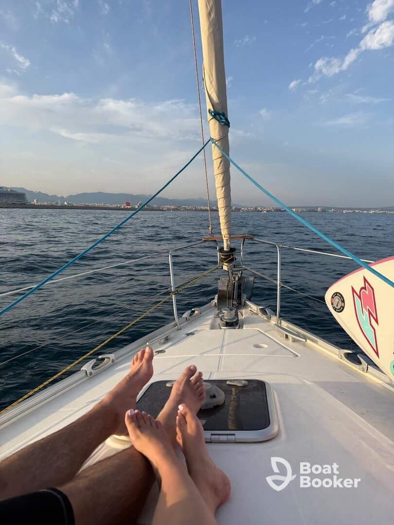A couple enjoys a relaxing moment on the bow of a sailboat, with their feet visible against the backdrop of a serene ocean and distant shoreline — perfect for romantic sailing adventures.