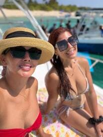 Two friends enjoy a sunny day on the deck of a boat, showcasing their vibrant beachwear and smiles — perfect for a fun day out on the water.