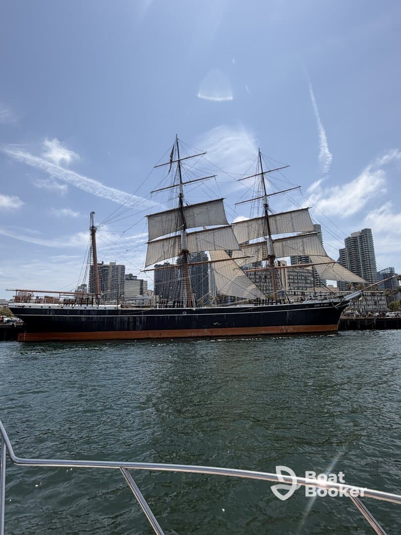 A majestic tall ship with sails raised, docked in a bustling harbor, showcasing classic maritime architecture against a clear blue sky.