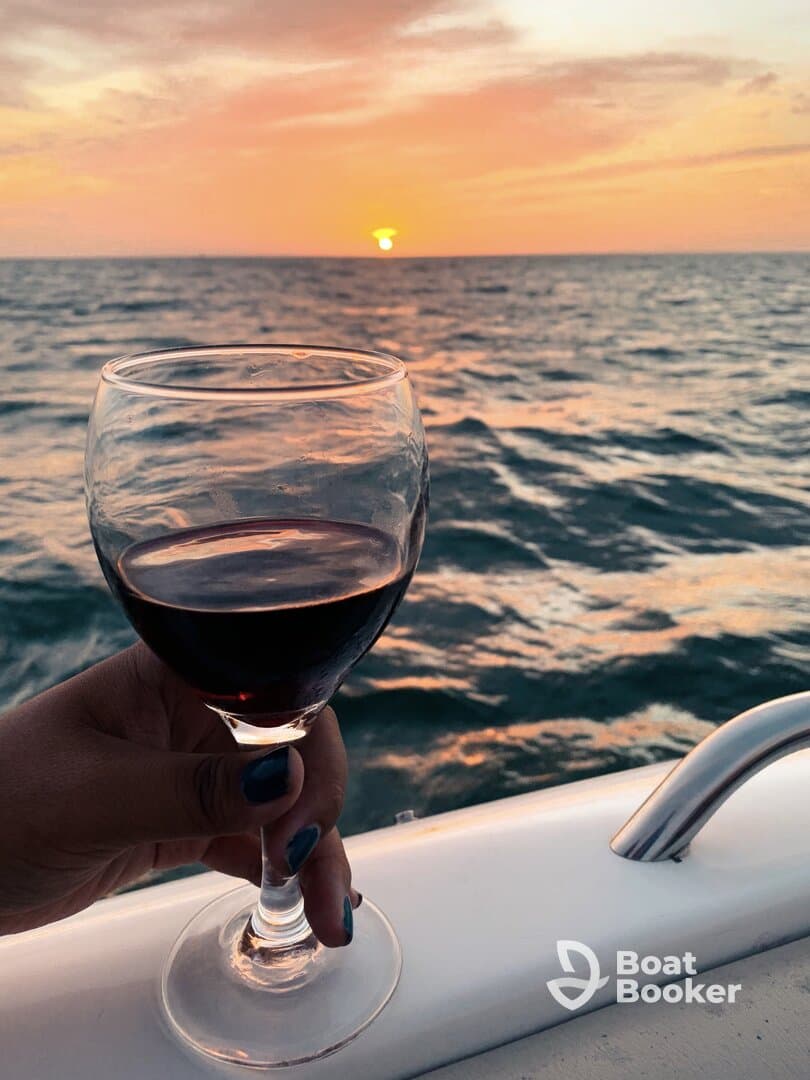 A hand holds a glass of red wine against a stunning sunset backdrop over the ocean, perfect for romantic evenings or sunset cruises.
