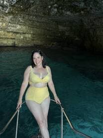 A woman poses on the edge of a boat in a stunning cave, showcasing the crystal-clear waters — a perfect moment for adventure seekers exploring hidden gems.