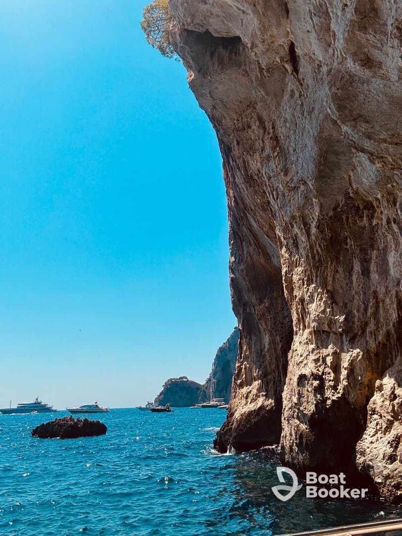 A stunning view of rocky cliffs and multiple boats anchored in the vibrant blue ocean, showcasing the natural beauty of the coastline.