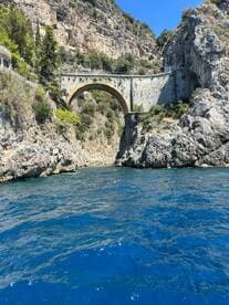 A stunning view of a historic bridge nestled among rocky cliffs, showcasing the breathtaking coastline and vibrant blue waters — a perfect representation of scenic boat tours.
