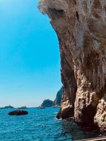 A stunning view of rocky cliffs and multiple boats anchored in the vibrant blue ocean, showcasing the natural beauty of the coastline.