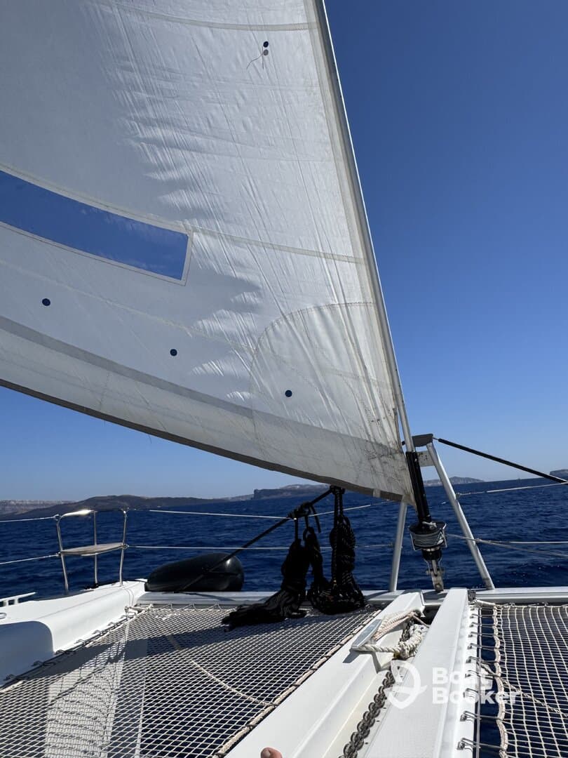 A close-up view of a sailboat's sail and deck, showcasing the vessel's structure as it navigates through open waters under a clear blue sky.