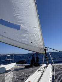 A close-up view of a sailboat's sail and deck, showcasing the vessel's structure as it navigates through open waters under a clear blue sky.