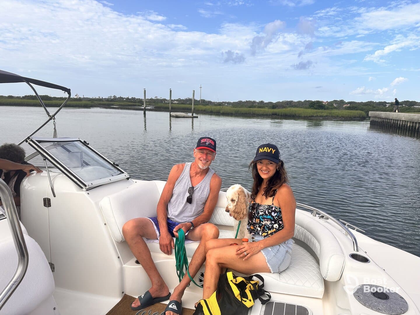 A couple enjoys a relaxing moment on their boat with a dog, surrounded by serene waters and lush greenery — perfect for a day out on the water.