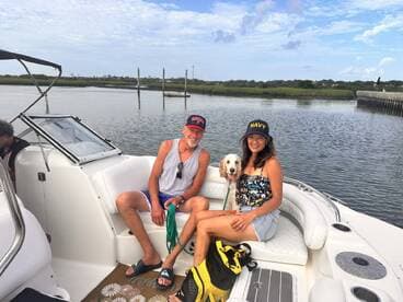 A cheerful group enjoys a relaxing moment on a boat with their dog, surrounded by scenic waters — perfect for a day of fun and companionship on the water.