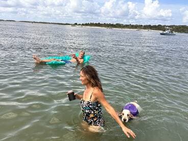 A fun day at the beach with friends, featuring a woman enjoying the water with her dog while a man relaxes on a float — perfect for summer outings.