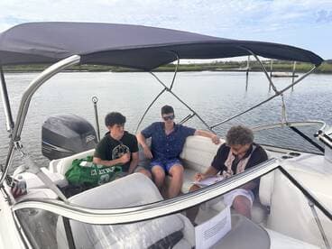 Three young men relax inside a boat's cabin, with one taking notes while the others enjoy the moment — a perfect setting for planning a day on the water.