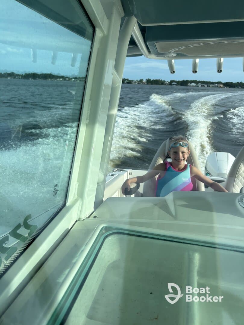A young girl enjoys a fun day on the water, steering a boat with a big smile — perfect for family adventures and creating lasting memories.
