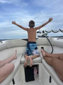 A joyful child spreads his arms wide on a boat, embracing the thrill of the ride — a perfect moment of fun and freedom on the water.